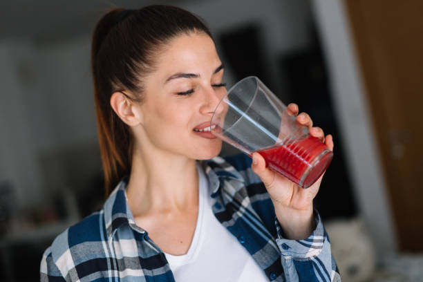 молодая женщина пьет сок. красивая женщина, держащая бутылку с красным соком. - women juice drinking breakfast стоковые фото и изображения