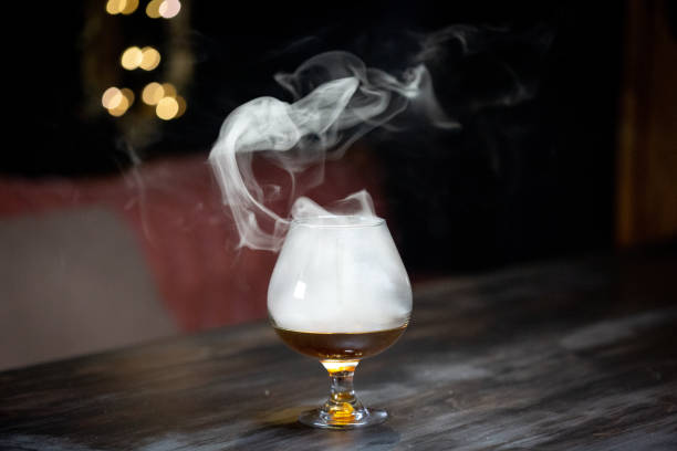 Smoking Cocktail Cognac cocktail billowing smoke as presentation. High end elegance in mixology. smoked stock pictures, royalty-free photos & images