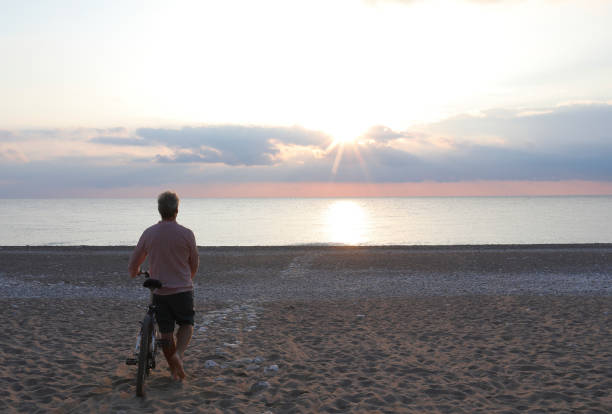 istock Mature man with bicycle relaxes on beach at sunrise 1187395423