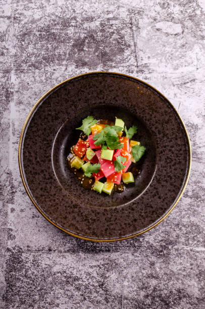 Top view raw tuna salad tartare with cucumber served on a black elegant plate on concrete background. Close up, table restaurant. Easy food for guests.