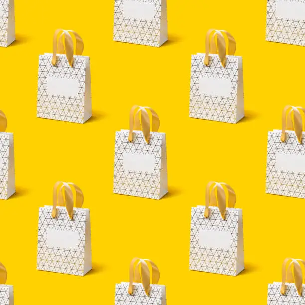 Photo of Seamless texture with White shopping bag on yellow background. Holiday sale concept, isometric view