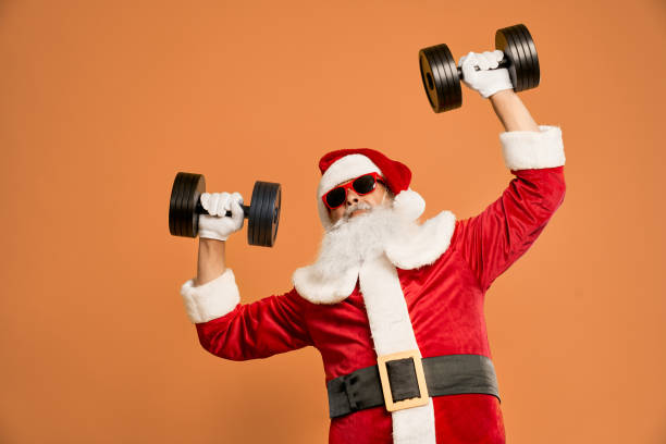 homme barbu drôle dans le costume de santa avec des haltères au-dessus de la tête - holiday healthy lifestyle weight christmas photos et images de collection