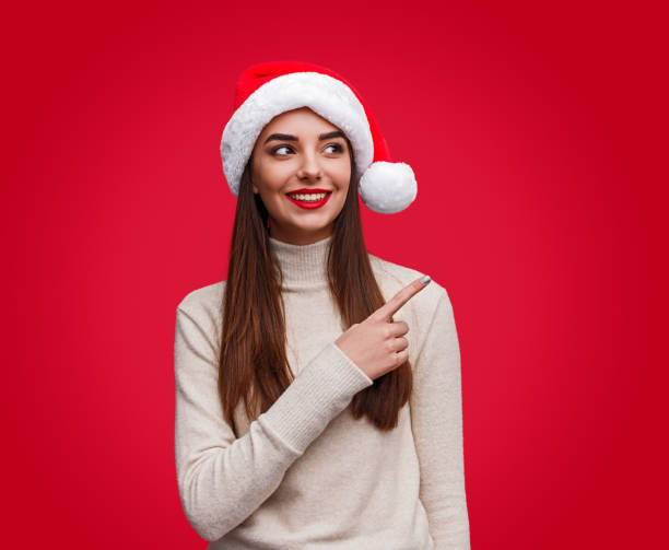 istock Cheerful young woman in Christmas hat pointing over shoulder 1187407019