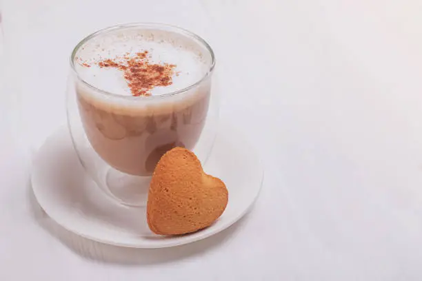 Hot latte in a glass cuo topped with cinnamon and a small heart shaped bisquit close-up