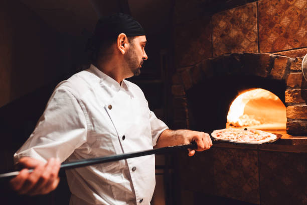 istock Chef putting the pizza in wood fired bread oven with a peel 1187411969