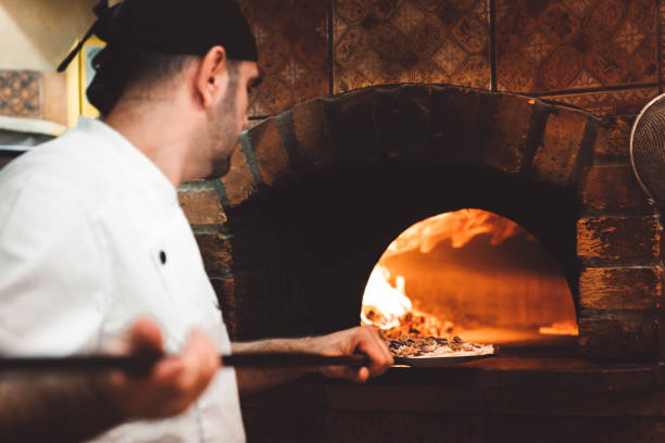 istock Pizza maker using a peel to put the pizza in a wood fire oven 1187412005