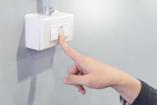 Male hand turning off the light when leaving. Pressing index finger on lighting switch panel control. Energy saving and environmental conservation concepts