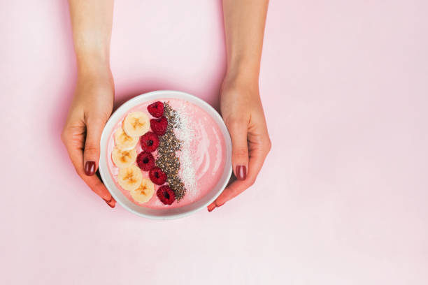 istock Woman's hands holding smoothie bowl with raspberries on pink background 1187420169