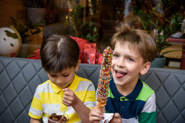 zwei kleine bruder junge essen waffel mit schokolade und bunten zucker streut im freien und fondue früchte. ungesundeleckeres süßigkeitenkonzept - child portrait fine art portrait multi colored stock-fotos und bilder