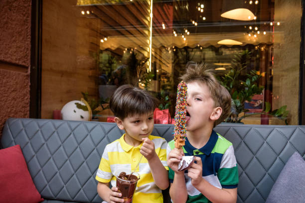 zwei kleine bruder junge essen waffel mit schokolade und bunten zucker streut im freien und fondue früchte. ungesundeleckeres süßigkeitenkonzept - child portrait fine art portrait multi colored stock-fotos und bilder