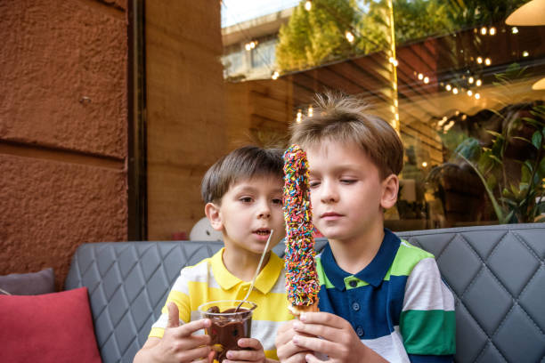 zwei kleine bruder junge essen waffel mit schokolade und bunten zucker streut im freien und fondue früchte. ungesundeleckeres süßigkeitenkonzept - child portrait fine art portrait multi colored stock-fotos und bilder