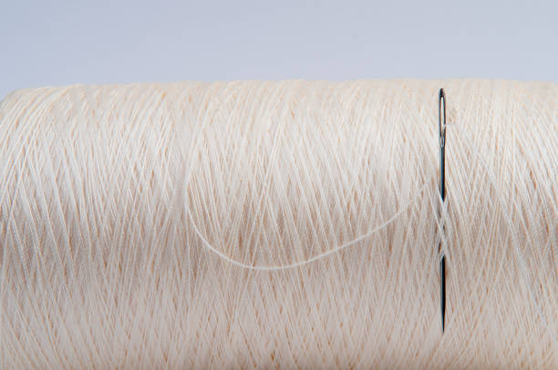 White spool of silk yarn with tucked needle on a blue background.