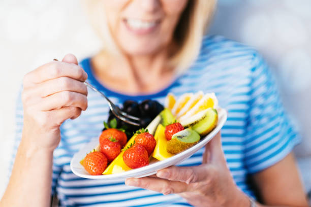 atractiva mujer mayor con almuerzo de frutas - fruit salad freshness strawberry fotografías e imágenes de stock