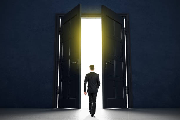 istock New life beginning concept with businessman entering open black doors in abstract bright space. 1187435234