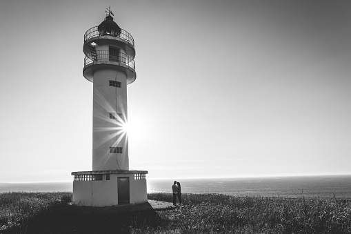 Couple in love outdoors, near a lighthouse and sthe sea. Monochrome version.