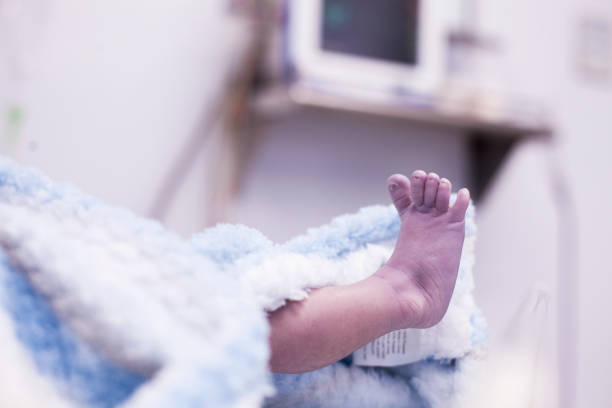 Newborn baby lying in her cloaked wrapper with her blue blanket stretches her leg and shows her little toes