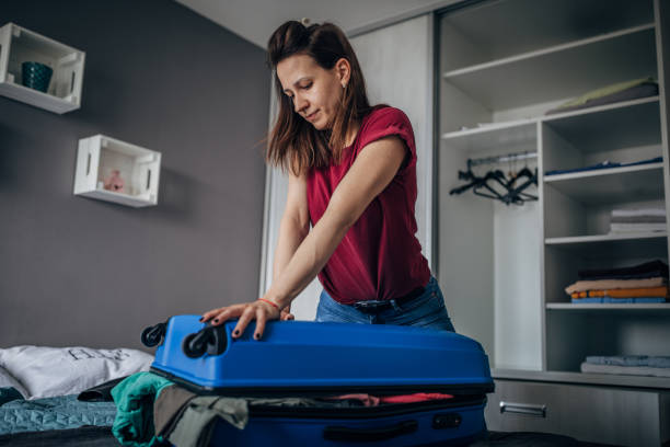 istock Young woman closing full suitcase 1187443196