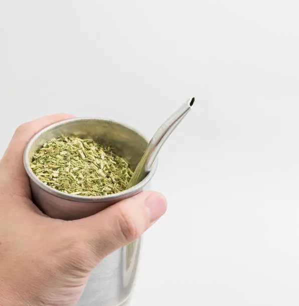 Hand holding a cup of Terere drink. Cold beverage typical from the midwest of brazil. Infusion of mate herb, Sul Mato Grossense beverage on a aluminum cup and the pump.