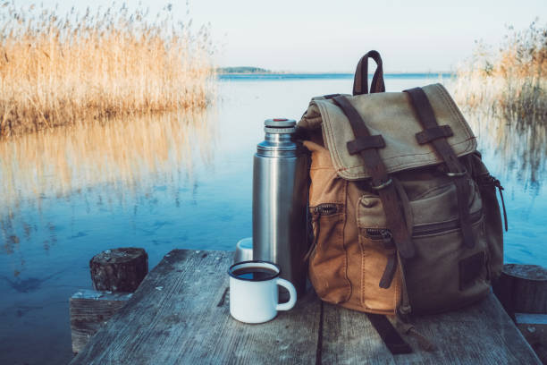 Enameled mug of coffee or tea, backpack of traveller and thermos on wooden pier on tranquil lake. Enameled mug of coffee or tea, backpack of traveller and thermos on wooden pier on tranquil lake. braslav lakes stock pictures, royalty-free photos & images