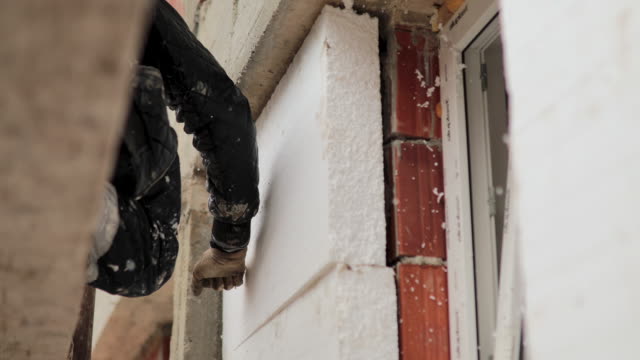 Man installing styrofoam insulation board for energy saving on exterior wall of house