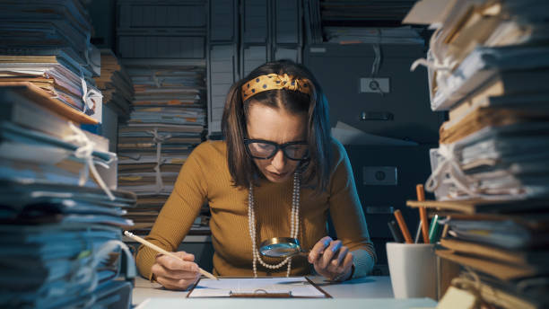 Businesswoman checking a contract with a magnifier Efficient businesswoman sitting at office desk and checking a contract with a magnifier, she is surrounded by piles of paperwork bureaucracy photos stock pictures, royalty-free photos & images
