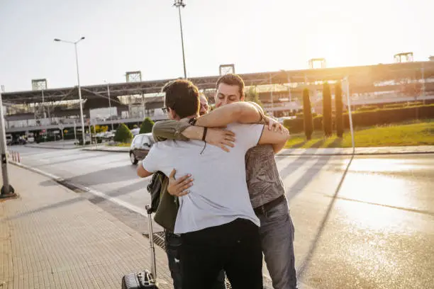 Two young men meeting friend on airport and give him big hug to welcome