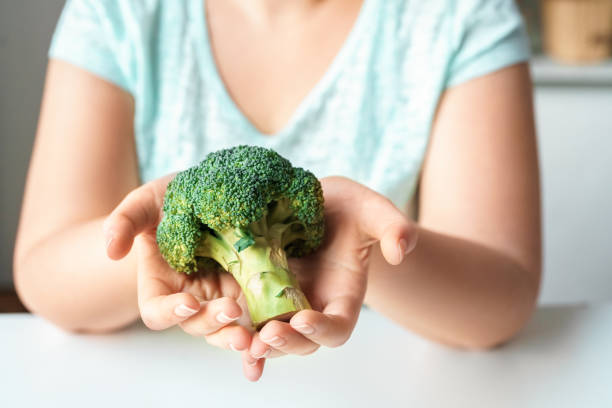 istock Body Care. Chubby girl sitting at kitchen table with broccoli close-up 1187482742
