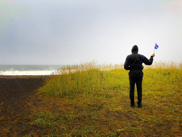 snaefellsnes, island: mann in raingear schwenkt isländische flagge - flag waving weather rain stock-fotos und bilder