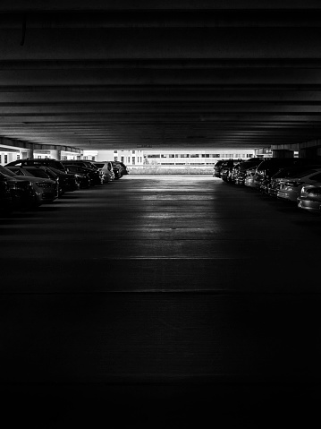 Dark parking garage deck with bright light at end of the row of cars - black and white photo