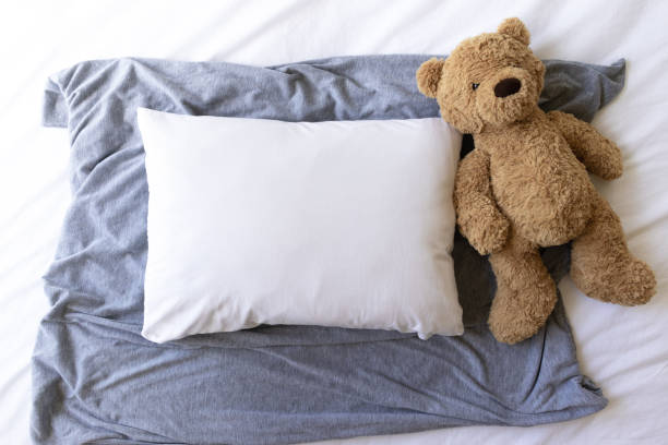 istock Blank white rectangle cushion laying on a grey scarf with a white background and childs teddy- nursery pillow mockup 1187498035