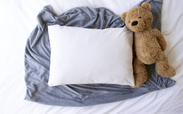 istock Blank white rectangle cushion laying on a grey scarf with a white background and childs teddy- nursery pillow mockup 1187498038