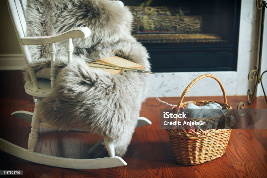 Basket with balls of yarn near chair and fireplace Blanket Stock Photo