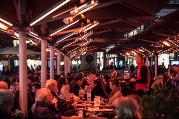 menschenmenge sitzt auf der terrasse eines vienna bar cafe und wird für den winter mit einer elektrischen heizung beheizt, die ein rotes licht erzeugt. - people winter urban scene chair stock-fotos und bilder