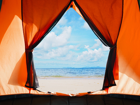 Looking through opening door of orange tent camping to summer beach background.
