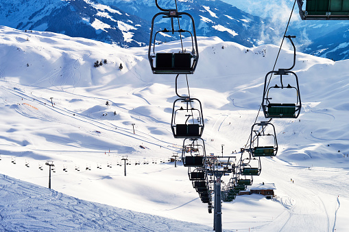 a large ski chair lift above a steep ski slope dotted with tracks on the snowy top of a high mountain in the Austrian Alps and a small chalet
