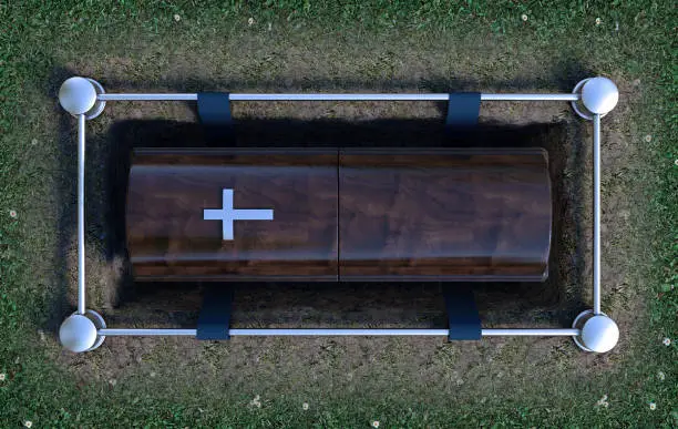 A modern wooden coffin at a funeral being lowered into a grave with a lowering mechanism a dirt and grass background - 3D Render