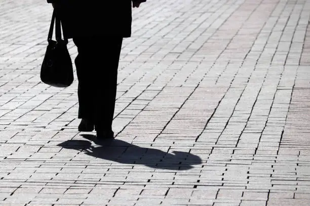 Photo of Silhouette of woman with bag walking down the street, black shadow on pavement