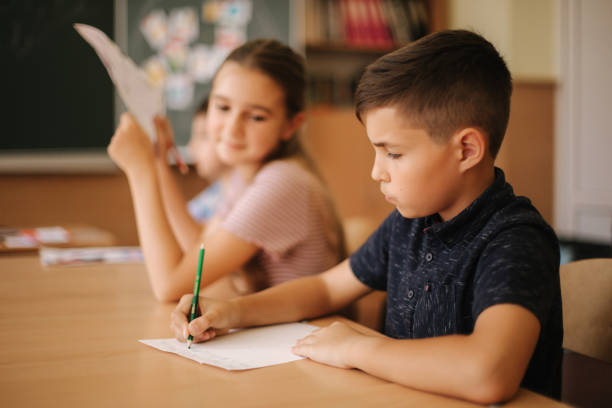 istock Group of school kids with pens and notebooks writing test in classroom. education, elementary school, learning and people concept 1187567613