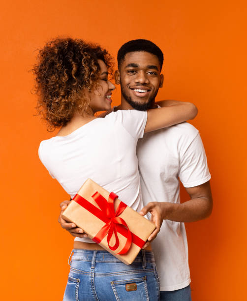 istock Black millennial couple with gift box on orange background 1187569667