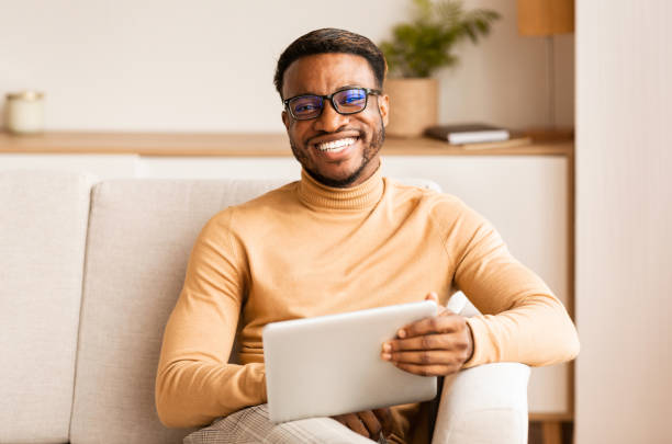 istock Young Afro Man Holding Tablet Computer Sitting On Couch Indoor 1187570072