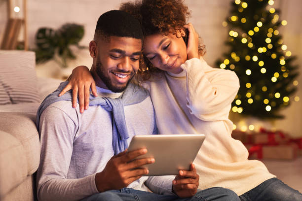 fröhliches schwarzes paar mit digitalem tablet gegen weihnachtsbaum - christmas shopping internet family stock-fotos und bilder
