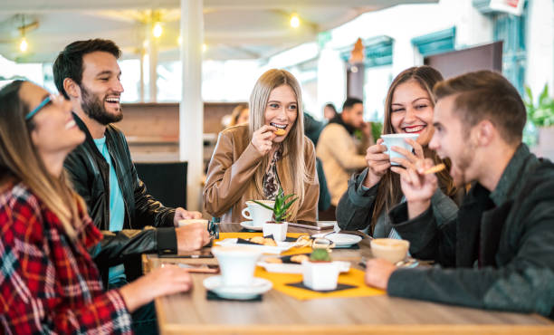 friends group drinking cappuccino at coffee bar - people talking and having fun together at fancy cafeteria - friendship concept with happy guys and girls at restaurant cafe - warm bulb light filter - breakfast eating people teens imagens e fotografias de stock