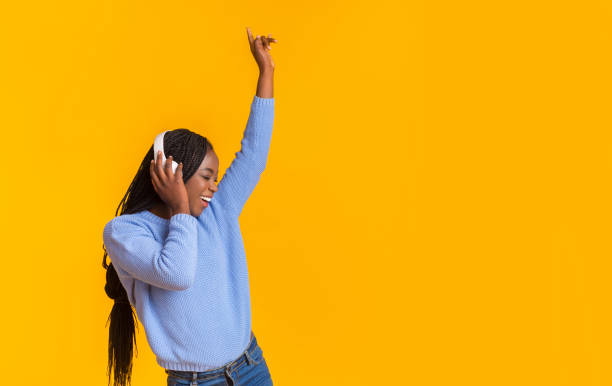 divertido afro chica disfrutando de la música, bailando sobre el fondo amarillo - vibrant color yellow recreational equipment red fotografías e imágenes de stock