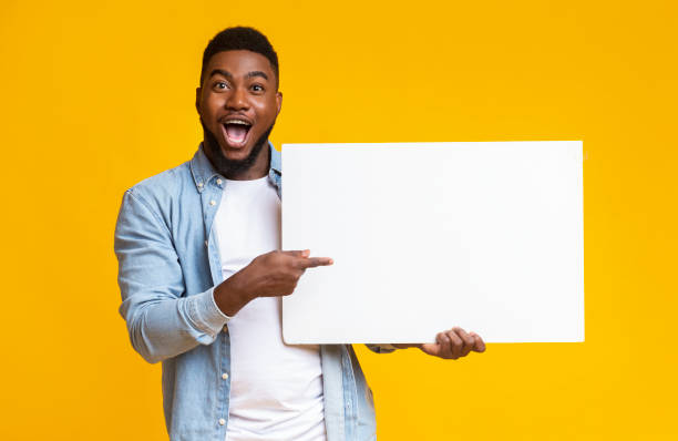 istock Joyful afro guy holding and pointing at white advertising board 1187574182