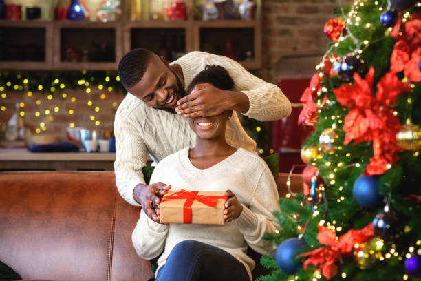 istock Black guy surprising wife with christmas gift, closing her eyes 1187574286