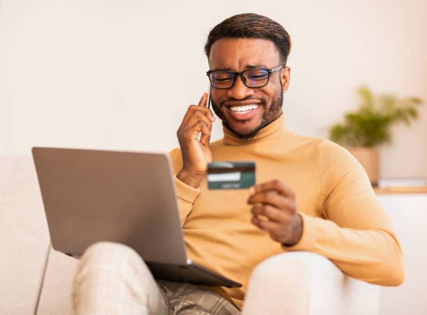 istock Man talking on cellphone using credit card and laptop indoor 1187574329