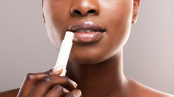 African american girl applying balm to her perfect plump lips, gray studio background, crop