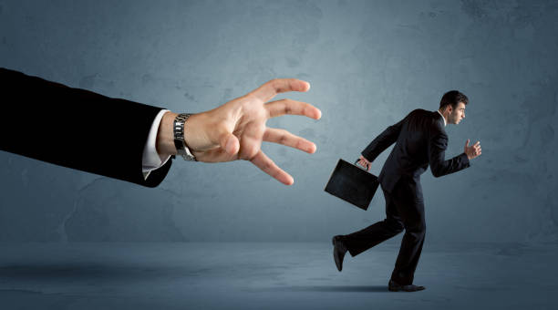 istock Business man running away from a huge hand concept 1187575613