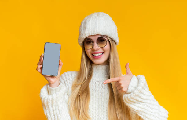 istock Woman in winter hat pointing at blank smartphone screen 1187575742