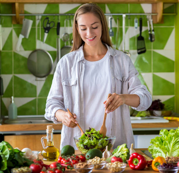 istock Young smiling woman making vegetable salad at home 1187576049